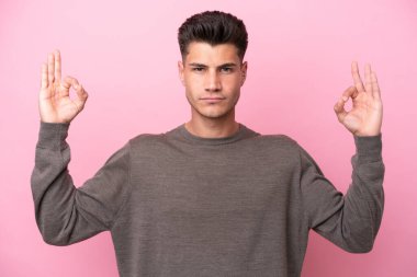 Zen pozisyonunda pembe arka planda izole edilmiş genç beyaz bir adam.