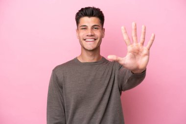 Pembe arka planda izole edilmiş genç beyaz adam parmaklarıyla beşi sayıyor.