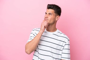 Pembe arka planda izole edilmiş genç beyaz adamın şüpheleri var.