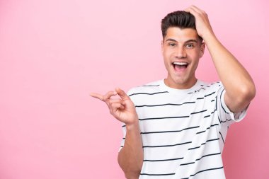 Pembe arka planda izole edilmiş genç beyaz adam şaşırmış ve parmağıyla kenarı işaret ediyor.