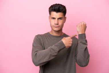 Pembe arka planda izole genç beyaz adam geç kalma jesti yapıyor.