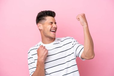 Pembe arka planda izole edilmiş genç beyaz bir adam zaferi kutluyor.