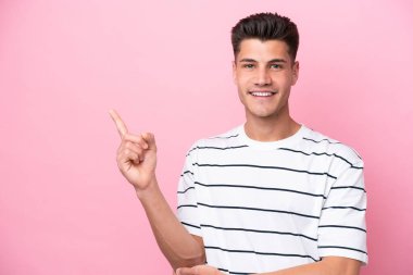 Pembe arka planda izole edilmiş genç beyaz adam mutlu ve yukarıya bakıyor.
