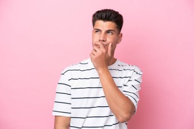 Pembe arka planda izole edilmiş genç beyaz adamın şüpheleri ve şaşkın bir yüz ifadesi var.