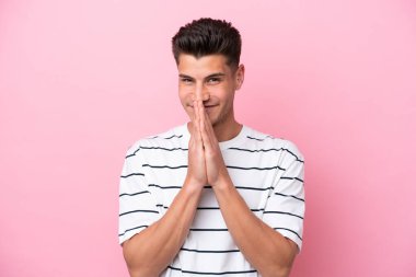 Pembe arka planda izole edilmiş genç beyaz adam avuç içlerini bir arada tutuyor. İnsan bir şey ister.