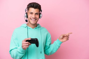 Pembe arka planda izole edilmiş bir bilgisayar oyunu kontrolörüyle oynayan yakışıklı beyaz bir adam.