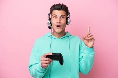 Pembe arka planda izole edilmiş bir bilgisayar oyunu kontrolörüyle oynayan yakışıklı beyaz adam çözümü bulmak için parmağını kaldırıyor.