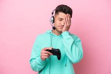 Pembe arka planda izole edilmiş, yorgun ve hasta bir ifadeyle video oyunu kontrolörüyle oynayan yakışıklı beyaz bir adam.