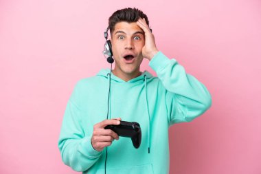 Pembe arka planda izole edilmiş bir bilgisayar oyunu kontrolörüyle oynayan yakışıklı beyaz bir adam.