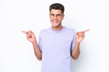 Beyaz arka planda izole edilmiş genç beyaz adam parmak uçlarını işaret ediyor ve mutlu.