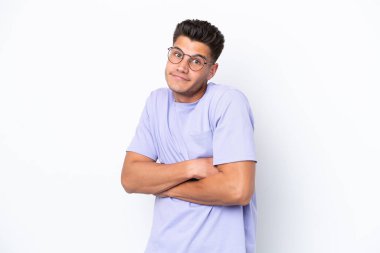 Beyaz arka planda izole olmuş genç beyaz bir adam omuzlarını kaldırırken şüpheyle hareket ediyor.