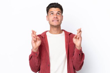 Beyaz arka planda izole olmuş genç beyaz bir adam parmaklarını çapraz yapıp en iyisini diliyor.