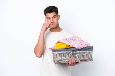 Çamaşır sepetini tutan beyaz arka planda izole edilmiş genç beyaz bir adam bir fikir düşünüyor.