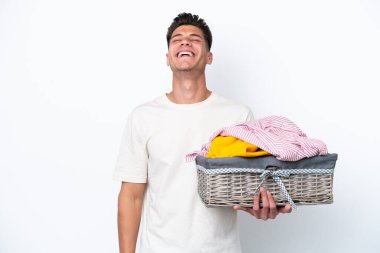 Beyaz arka planda çamaşır sepetini tutan genç beyaz adam gülüyor.