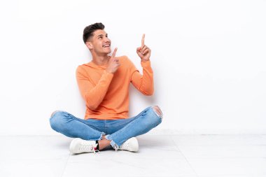 Beyaz arka planda izole bir şekilde yerde oturan genç adam işaret parmağıyla işaret etmek harika bir fikir.