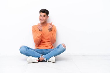 Yerde oturan genç adam, beyaz arka planda izole bir şekilde para hareketi yapıyor.