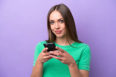 Mor arka planda izole edilmiş genç beyaz kadın cep telefonuyla bir mesaj gönderiyor.