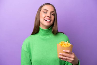 Mor arka planda kızarmış patates kızartması tutan genç beyaz kadın gülüyor.