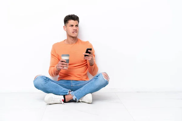 Joven Sentado Suelo Aislado Sobre Fondo Blanco Sosteniendo Café Para —  Fotos de Stock