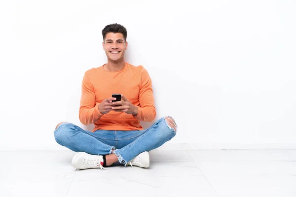 Jovem Sentado Chão Isolado Fundo Branco Enviando Uma Mensagem Com — Fotografia de Stock