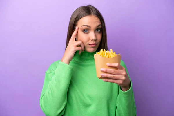 Giovane Donna Caucasica Possesso Patatine Fritte Sfondo Viola Pensando Idea — Foto Stock