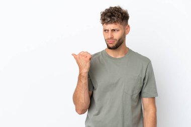 Beyaz arka planda izole edilmiş beyaz, yakışıklı genç adam mutsuz ve kenarı işaret ediyor.
