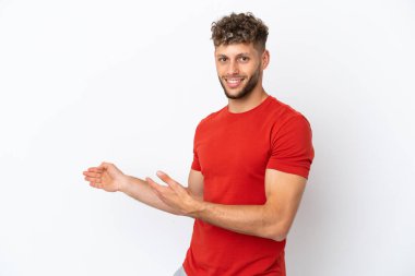 Beyaz arka planda soyutlanmış beyaz tenli yakışıklı adam, davet edilmek için ellerini yana uzatıyor.