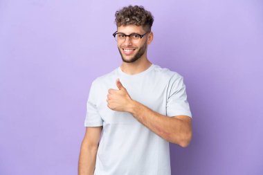 Teslimatçı beyaz adam mor arka planda izole edilmiş bir şekilde baş parmak işareti yapıyor.