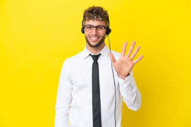 Sarı arka planda izole edilmiş kulaklıkla çalışan pazarlamacı sarışın adam beş parmaklı sayıyor.