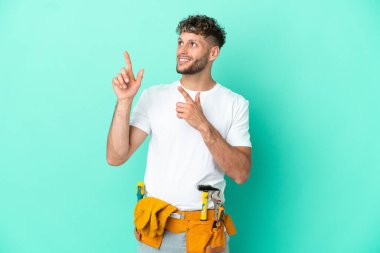 Genç elektrikçi sarışın adam yeşil arka planda izole edilmiş işaret parmağıyla işaret etmek harika bir fikir.