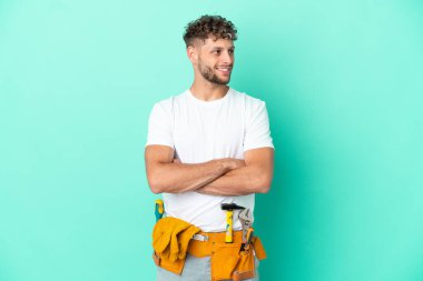 Genç elektrikçi sarışın adam yeşil arka planda izole edilmiş mutlu ve gülümsüyor.