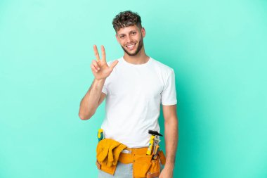 Genç elektrikçi sarışın adam yeşil arka planda izole edilmiş mutlu ve parmaklarıyla üçe kadar sayıyor.