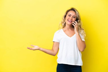 Sarı arka planda izole edilmiş genç Brezilyalı bir kadın cep telefonuyla sohbet ediyor.