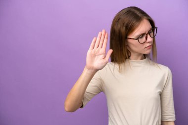 Mor arka planda izole edilmiş genç bir İngiliz kadın dur hareketi yapıyor ve hayal kırıklığına uğruyor