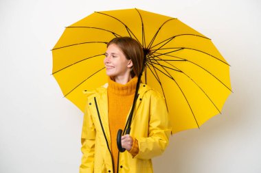 Yağmura dayanıklı ceketi ve şemsiyesi olan genç İngiliz kadın beyaz arka planda izole edilmiş.