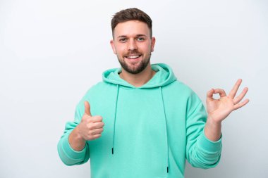 Beyaz arka planda izole edilmiş genç beyaz bir adam Tamam işareti ve baş parmak işareti