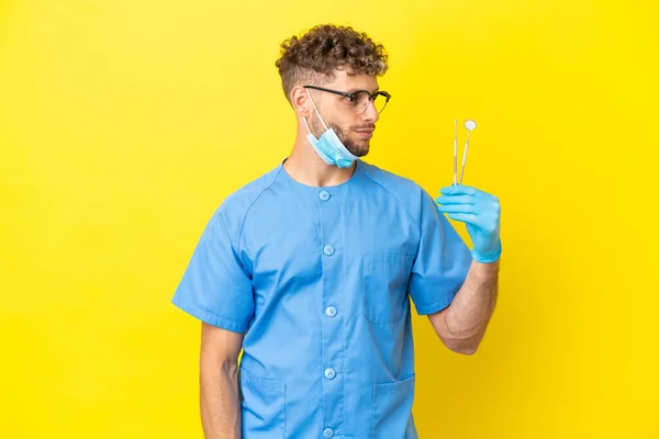 Dentista Loira Homem Segurando Ferramentas Isoladas Fundo Olhando Para Lado — Fotografia de Stock