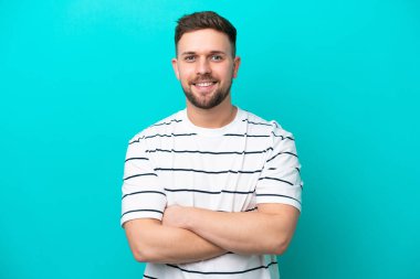 Mavi arka planda izole genç beyaz adam kollarını ön pozisyonda çapraz tutuyor.
