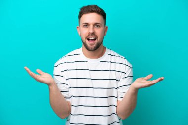 Kafkasyalı genç adam mavi arka planda izole edilmiş ve şok olmuş yüz ifadesi var.