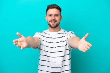 Mavi arka planda izole edilmiş genç beyaz adam sunar ve davet eder.