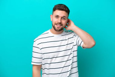 Kafkasyalı genç adam mavi arka planda tek başına gülüyor.