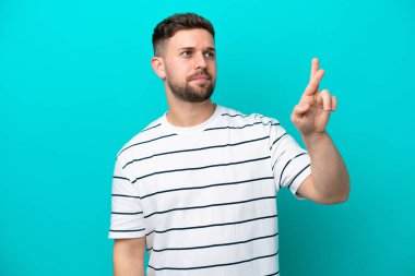 Kafkasyalı genç adam mavi arka planda izole edilmiş, şans diliyor ve en iyisini diliyor.