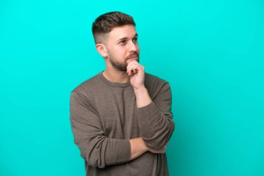 Kafkasyalı genç adam mavi arka planda izole edilmiş bir şekilde yukarı bakarken bir fikir düşünüyor.