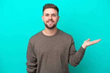 Mavi arka planda izole edilmiş genç beyaz adam bir ilan vermek için avucunun içinde hayali bir fotokopi makinesi tutuyor.