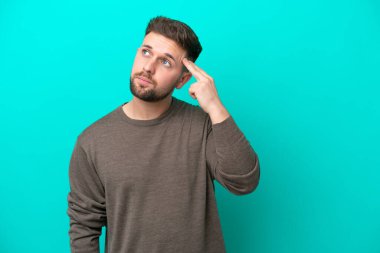 Genç beyaz adam mavi arka planda izole edilmiş ve intihar jesti yapmada sorun yaşıyor.