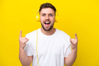 Kafkasyalı genç adam sarı arka planda izole edilmiş rock hareketleri yapan müzik dinliyor.