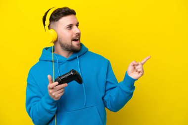 Sarı arka planda izole edilmiş bir bilgisayar oyunu kontrolörüyle oynayan genç beyaz adam çözümü fark ederken parmağını kaldırmayı amaçlıyor.