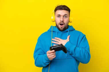 Sarı arka planda izole edilmiş bir bilgisayar oyunu kontrolörüyle oynayan beyaz bir adam sağa bakarken şaşırmış ve şok olmuştu.