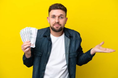 Kafkasyalı genç adam sarı arka planda izole edilmiş bir sürü para alıyor.