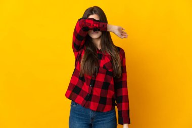 Genç Brezilyalı kız sarı arka planda izole edilmiş gözleri elleriyle kapatıyor.